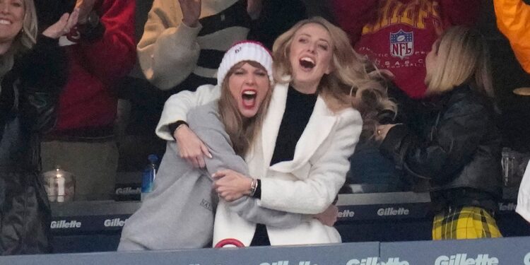 Taylor Swift in a grey sweatshirt excitedly hugs Brittany Mahomes in a white jacket