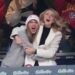 Taylor Swift in a grey sweatshirt excitedly hugs Brittany Mahomes in a white jacket