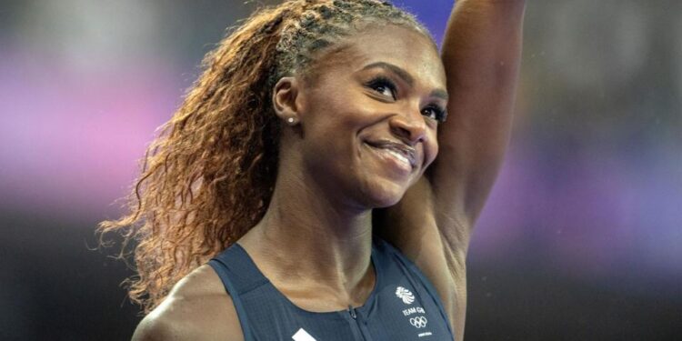 A smiling Dina Asher-Smith raises her left arm in a salute