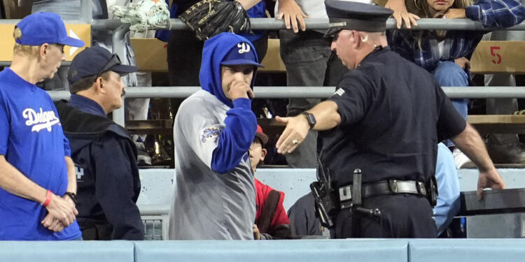 A law enforcement officer talks with a fan who reached over the outfield wall to catch a fly ball by New York Yankees' Gleyber Torres during the ninth inning in Game 1 of the baseball World Series, Friday, Oct. 25, 2024, in Los Angeles. (AP Photo/Godofredo A. Vásquez)