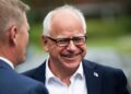 Tim Walz, man with white hair, smiling with black rimmed glasses