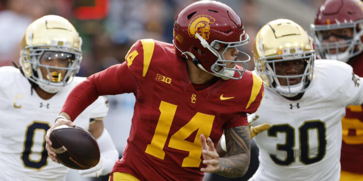 LOS ANGELES, CALIFORNIA - NOVEMBER 30: Quarterback Jayden Maiava #14 of the USC Trojans is chased out of the pocket by safety Xavier Watts #0 and defensive lineman Bryce Young #30 of the Notre Dame Fighting Irish during the first half at United Airlines Field at the Los Angeles Memorial Coliseum on November 30, 2024 in Los Angeles, California. (Photo by Kevork Djansezian/Getty Images)