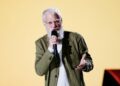 David Letterman in an olive green jacket speaks with his hands on stage