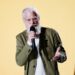 David Letterman in an olive green jacket speaks with his hands on stage