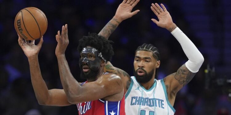 Philadelphia 76ers' Joel Embiid, left, tries to pass against Charlotte Hornets' Nick Richards during the first half of an NBA basketball game, Friday, Dec. 20, 2024, in Philadelphia. (AP Photo/Matt Slocum)