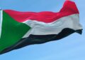 Palestinian flag flying atop a flagpole against a blue sky