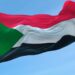 Palestinian flag flying atop a flagpole against a blue sky