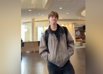Student in beige winter jacket standing in campus building