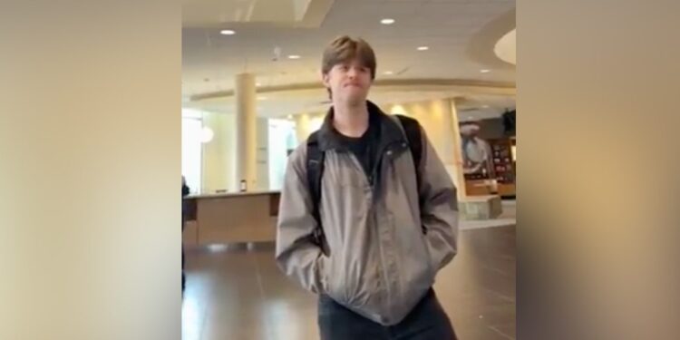 Student in beige winter jacket standing in campus building