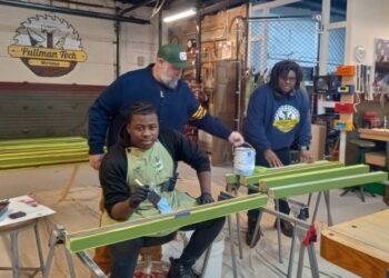 Pullman Tech Workshop founder Nick Lubovich delivers paint to La'Shawn Smith, left, who is now part of the Workshop's Advanced Workforce Development Training program, and assistant instructor Donovan Parks, as they work painting part of the porch for a home in Pullman during a recent session at the workshop along Front Street between Roseland and Pullman. (Janice Neumann/Daily Southtown)