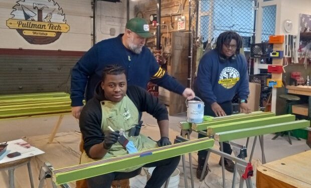 Pullman Tech Workshop founder Nick Lubovich delivers paint to La'Shawn Smith, left, who is now part of the Workshop's Advanced Workforce Development Training program, and assistant instructor Donovan Parks, as they work painting part of the porch for a home in Pullman during a recent session at the workshop along Front Street between Roseland and Pullman. (Janice Neumann/Daily Southtown)