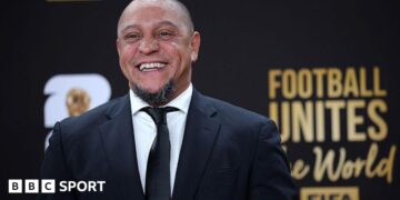Roberto Carlos smiles for a photo while wearing a suit at the Fifa World Cup draw