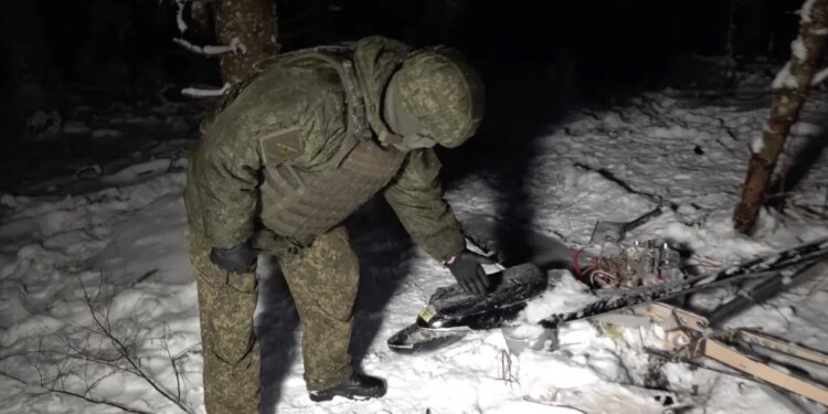 Russian soldier standing over drone wreckage in snow