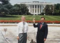 Assistant Curator William G. Allman and Gary J. Walters hold a gold ball and laugh in front of the White House.