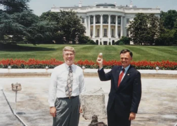 Assistant Curator William G. Allman and Gary J. Walters hold a gold ball and laugh in front of the White House.