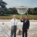 Assistant Curator William G. Allman and Gary J. Walters hold a gold ball and laugh in front of the White House.