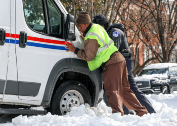 People help push a USPS truck out of snow and ice, two days after a winter storm in Washington
