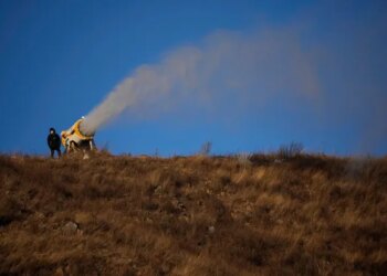 A person works at a snow making machine on a hill overlooking cross-country skiing practice before the 2022 Winter Olympics, Feb. 2, 2022, in Zhangjiakou, China. (AP Photo/Aaron Favila, File)