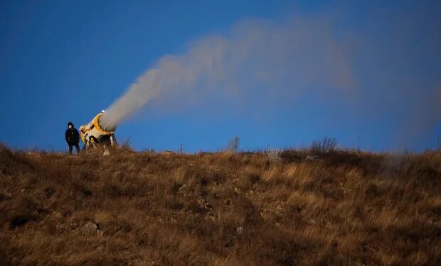 A person works at a snow making machine on a hill overlooking cross-country skiing practice before the 2022 Winter Olympics, Feb. 2, 2022, in Zhangjiakou, China. (AP Photo/Aaron Favila, File)