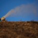 A person works at a snow making machine on a hill overlooking cross-country skiing practice before the 2022 Winter Olympics, Feb. 2, 2022, in Zhangjiakou, China. (AP Photo/Aaron Favila, File)
