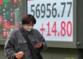 A person walks in front of an electronic stock board showing Japan's Nikkei index.