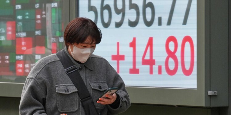 A person walks in front of an electronic stock board showing Japan's Nikkei index.
