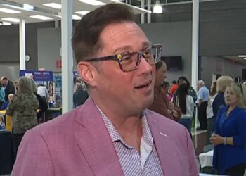 Chad Alan-Carr wearing glasses and pink suit during an interview