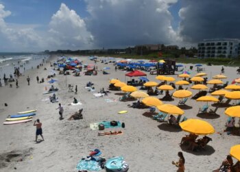 Beachgoers sitting and standing on Cocoa Beach with umbrellas
