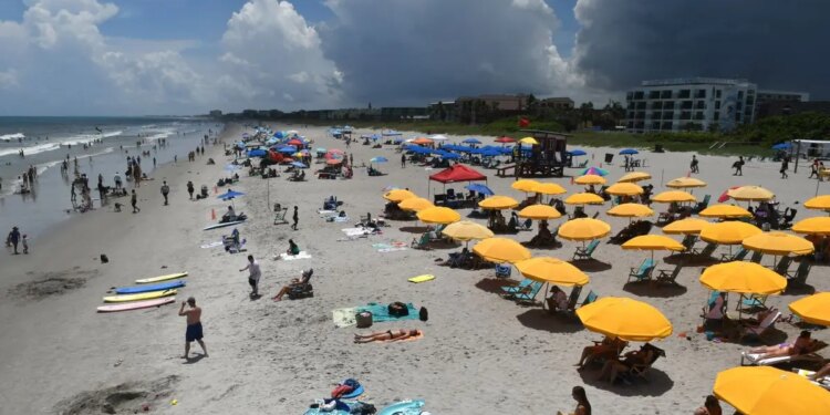 Beachgoers sitting and standing on Cocoa Beach with umbrellas