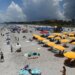 Beachgoers sitting and standing on Cocoa Beach with umbrellas