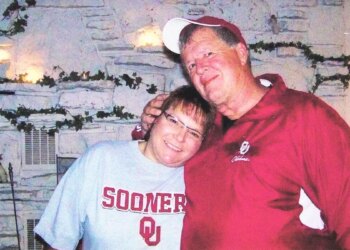 Deb Proctor in a grey college shirt being held by Jeff Walton in a red jacket.