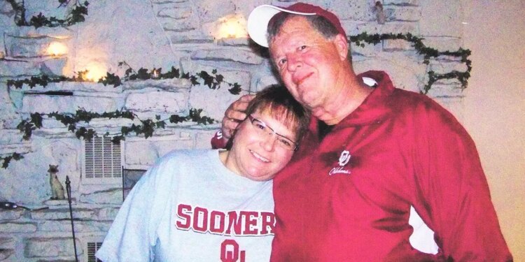 Deb Proctor in a grey college shirt being held by Jeff Walton in a red jacket.