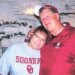 Deb Proctor in a grey college shirt being held by Jeff Walton in a red jacket.