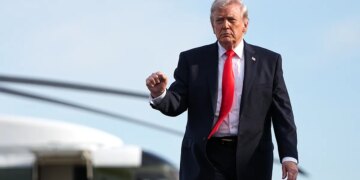 President Donald Trump walking from the Marine One helicopter toward Air Force One at an airport.