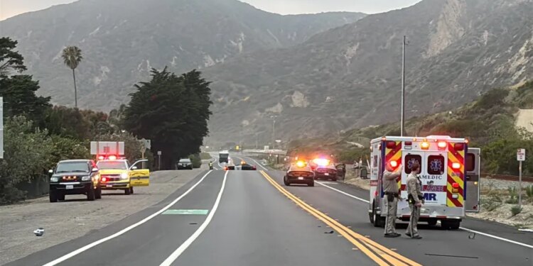 California Highway Patrol officers, an ambulance and emergency vehicles are seen at the scene of a fatal crash involving three bicyclists and a pickup truck on Pacific Coast Highway near Solimar Beach Road in Ventura County, with mountains in the background.