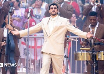 Bad Bunny in the centre with musicians surrounding him and a crowd in the background