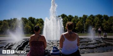Two women look at a fountain on a sunny day with their backs to the camera