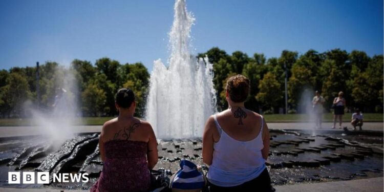 Two women look at a fountain on a sunny day with their backs to the camera