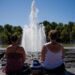 Two women look at a fountain on a sunny day with their backs to the camera