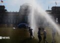 People pass by a watering system in front of the Reichstag on a hot summer day on June 24, 2026