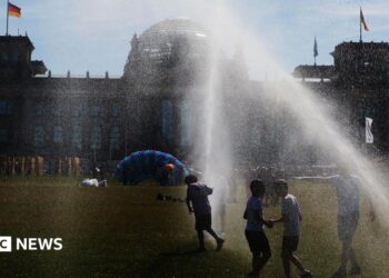 People pass by a watering system in front of the Reichstag on a hot summer day on June 24, 2026