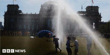 People pass by a watering system in front of the Reichstag on a hot summer day on June 24, 2026