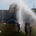 People pass by a watering system in front of the Reichstag on a hot summer day on June 24, 2026