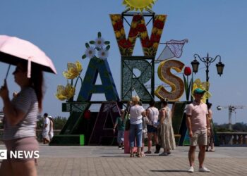 A woman walks under an umbrella past a "Warsaw" sign as a heatwave sweeps Poland, in Warsaw, Poland,