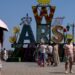A woman walks under an umbrella past a "Warsaw" sign as a heatwave sweeps Poland, in Warsaw, Poland,