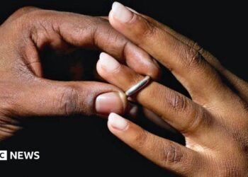A man places a silver wedding band onto a young woman's ring finger.