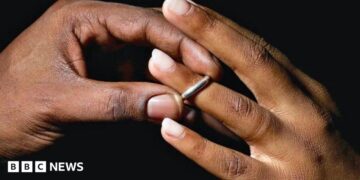 A man places a silver wedding band onto a young woman's ring finger.