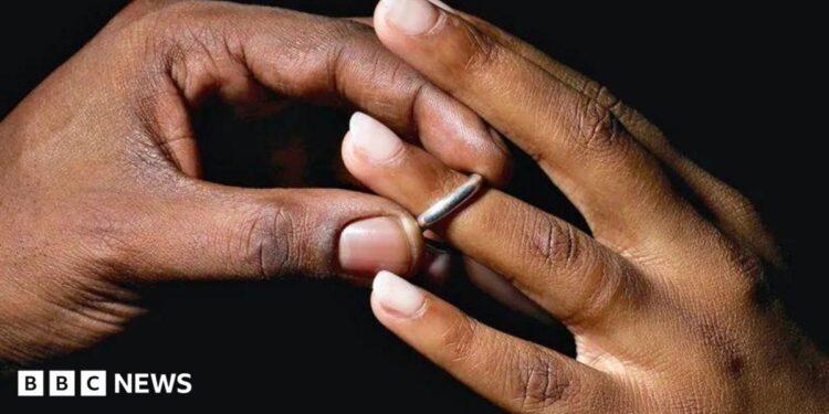 A man places a silver wedding band onto a young woman's ring finger.