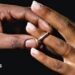 A man places a silver wedding band onto a young woman's ring finger.