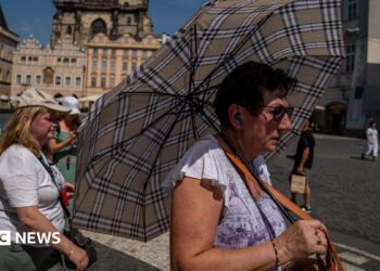 A woman with an umbrella shields herself from the sun in Prague's Old Town